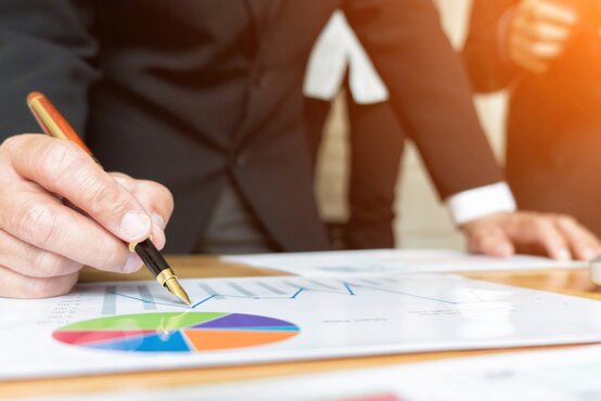 Businessman in a suit analyses investment charts and financial reports with a pen at his desk in a modern office