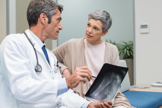 Doctor in a white coat with a stethoscope explains an X-ray to a patient in a modern consultation room.