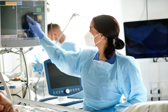 Medizinisches Fachpersonal in Schutzkleidung überwacht Vitaldaten an Patientenmonitor auf Intensivstation.